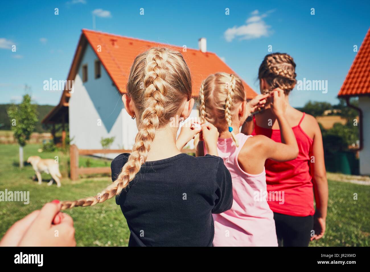Girls each to other making hair braids of the little girl on the garden in the countryside. Stock Photo