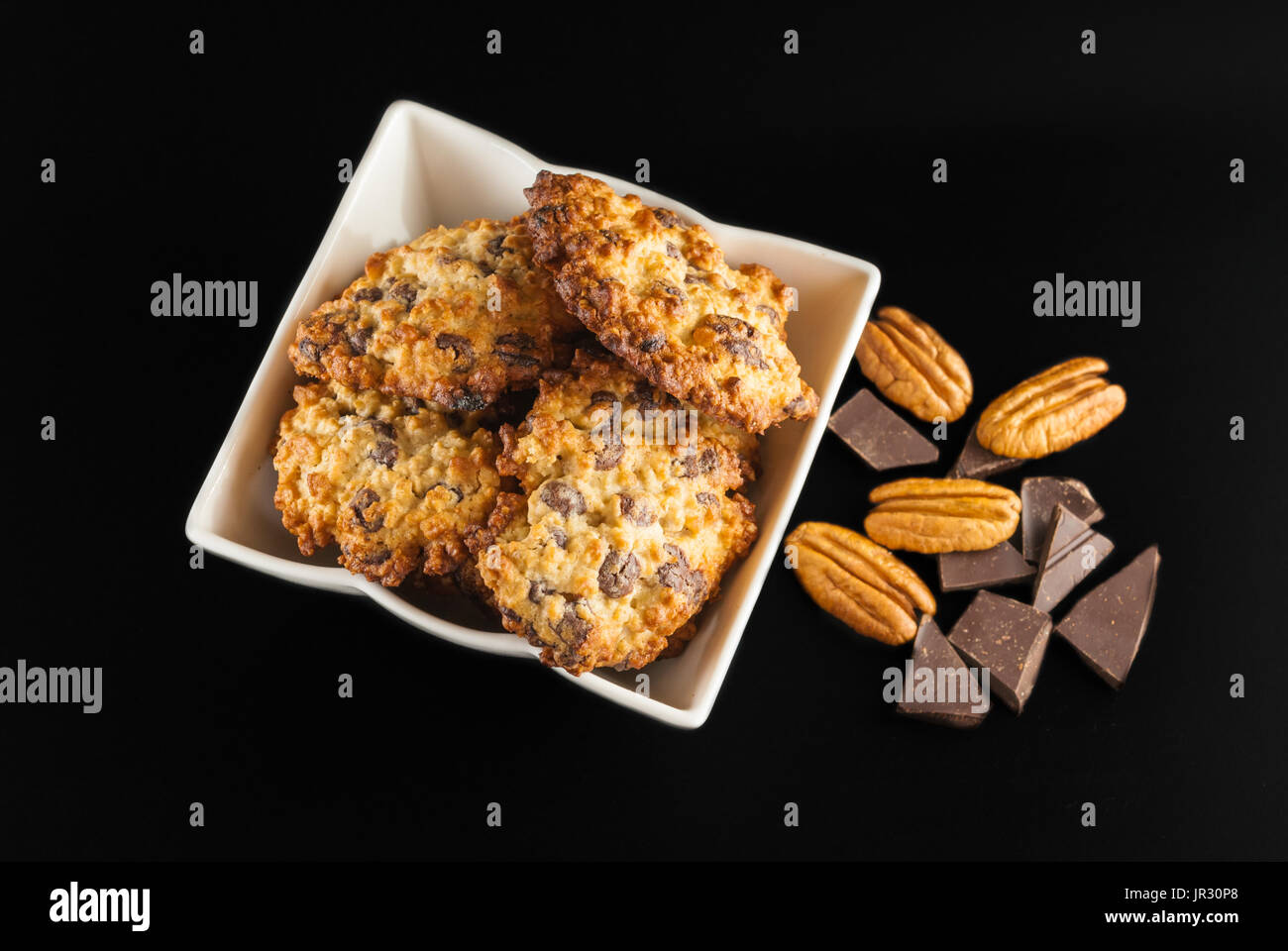 Chocolate chip cookies in a white bowl, pecan nuts and pieces of chocolate, top view,  on a black background Stock Photo