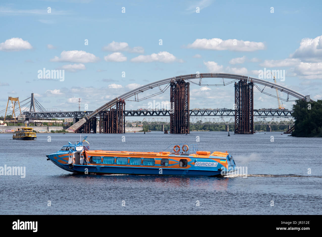 KYIV, UKRAINE - JUNE 12, 2016:  Tourist Excursion boat on the Dnieper (Dnipro) River with the Podilsko-Voskresensky Bridge in the background Stock Photo