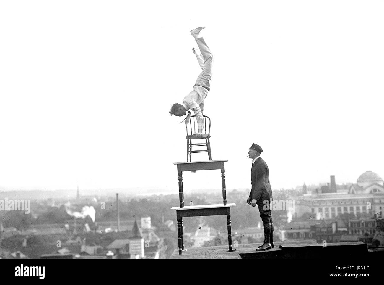 Reynolds performing acrobatic and balancing acts on high cornice above 9th Street, N.W. Washington, DC. John 'Jammie' Reynolds (born 1890 or 91 - ?) was an American daredevil. Little is known about early life, what became of him once he stopped performing or even his real name. An acrobat and juggler, he was known by many names - Daredevil Johnny, Daredevil Jack, the Climbing Wonder, The Lizard, the Human Spider, and the Human Fly. A newspaper article from 1922 claims he began performing at the age six in Buffalo, balancing on one foot from a flagpole 140 feet in the air. His first major stunt Stock Photo
