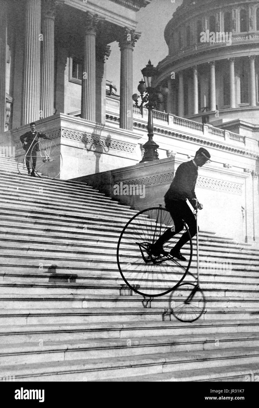 Man riding a bicycle down the steps of the US Capitol as another man with a bicycle waits at the top. Photographed by the Platt Brothers, 1884. Stock Photo