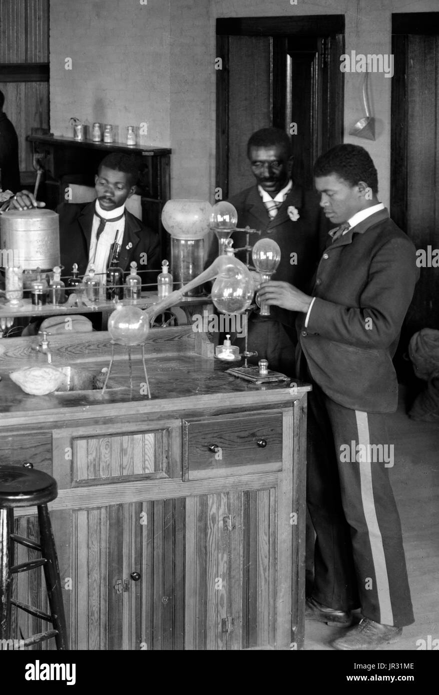 Chemistry laboratory/classroom with students at the Tuskegee Institute, Tuskegee, Alabama. George Washington Carver stands second from right, facing front (framed by doorway). George Washington Carver (1864 - January 5, 1943) was an African-American scientist, botanist, educator, and inventor born into slavery. In 1891 he attended and studied botany at Iowa State Agricultural College where he was the first black student, and later taught as the first black faculty member. His reputation is based on his research into and promotion of alternative crops to cotton, such as peanuts, soybeans and sw Stock Photo