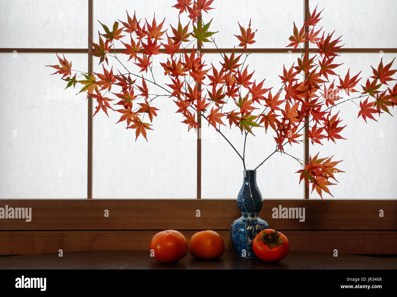 Rustic autumn scene of red Japanese maple leaves and ripe persimmons in front of a rice paper window background Stock Photo