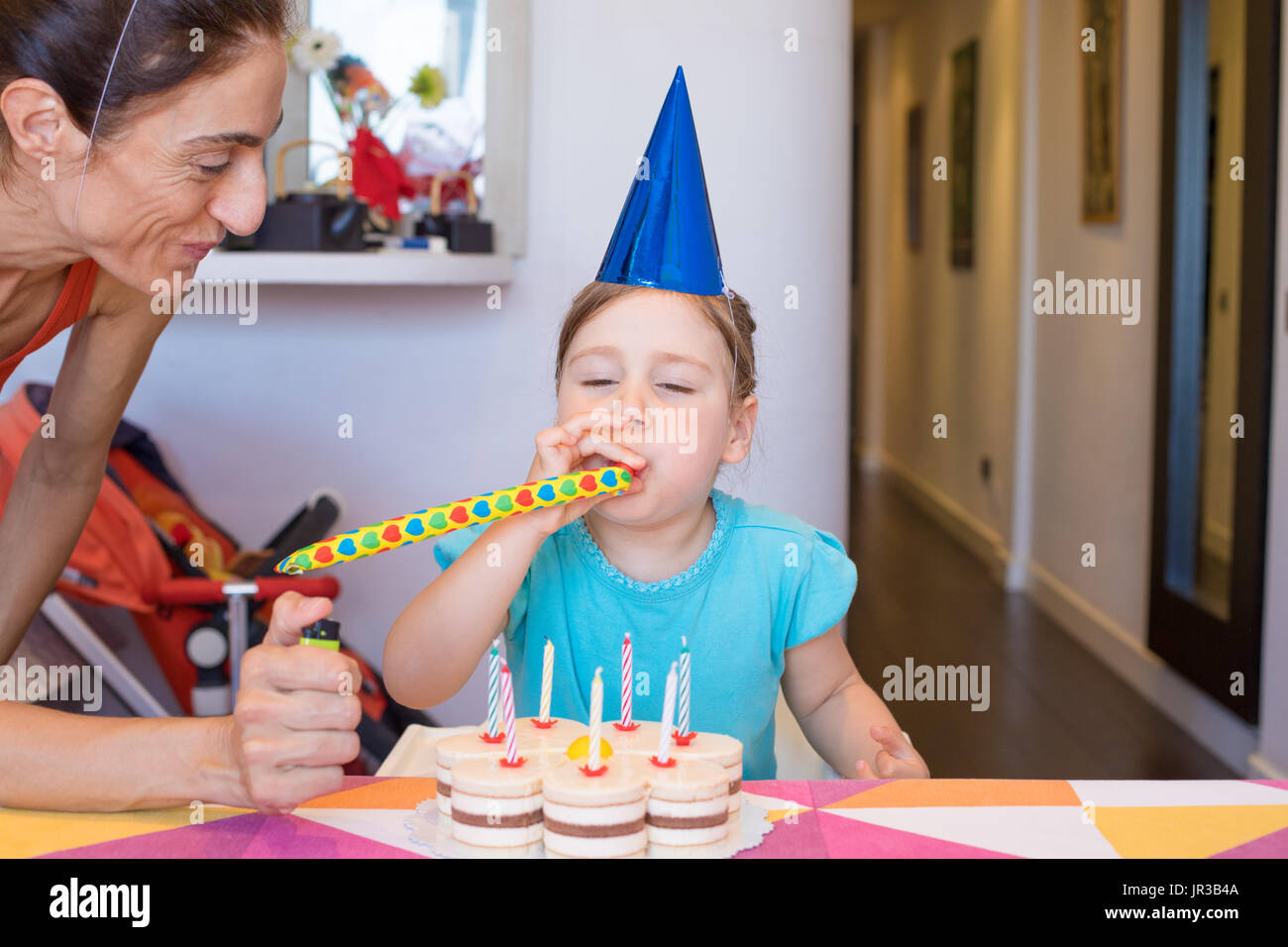 three years old blonde child, with blue cone hat, blowing a party