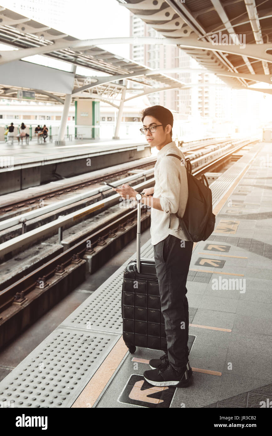 Man is on the train station with travel bag, using mobile phone, wait for a train Stock Photo