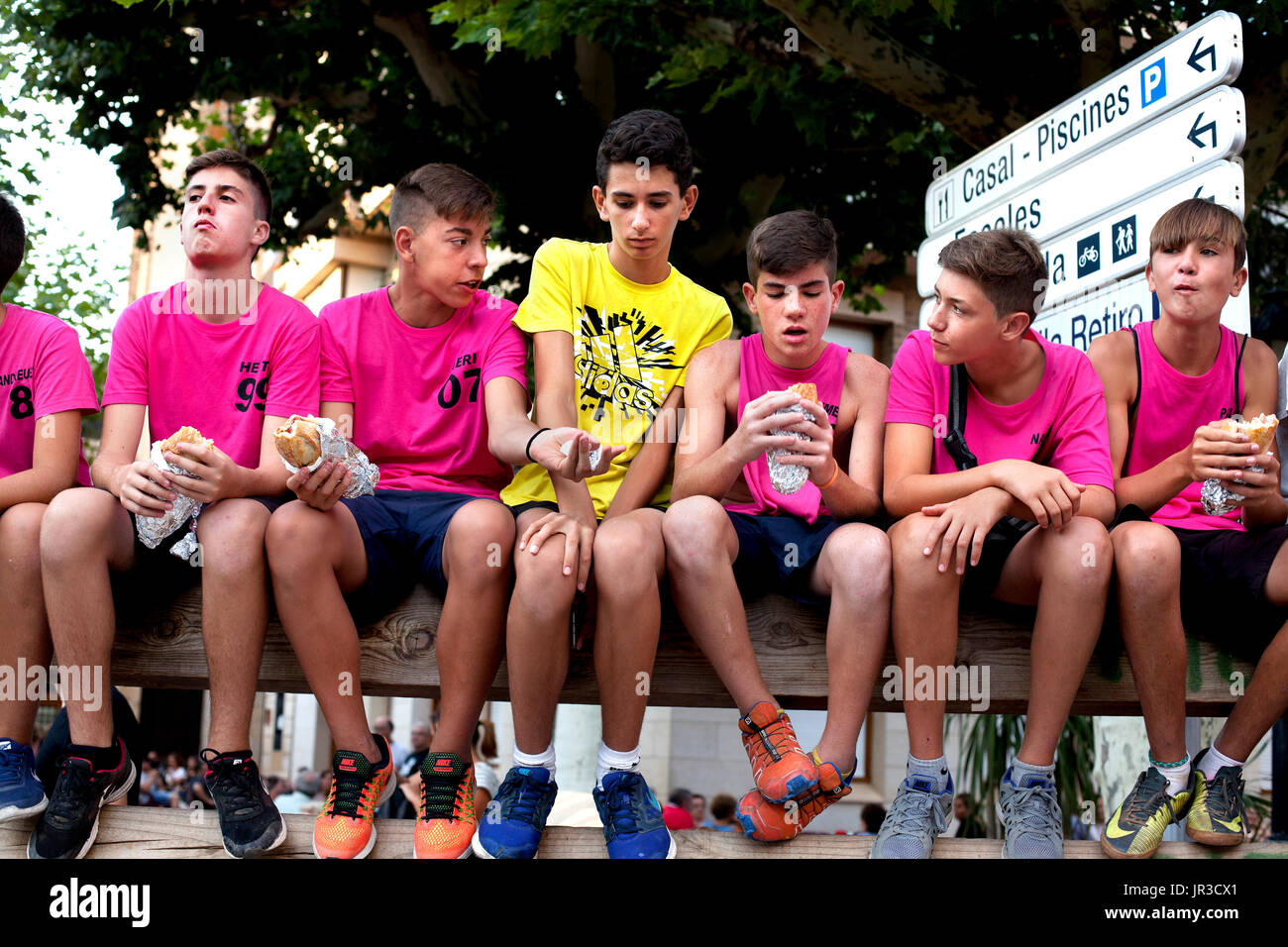 Tenage boys sit up on a barrier waiting for the first bulls to be released into the town for the annual summer bull running event, Cherta , Tarragona. Stock Photo