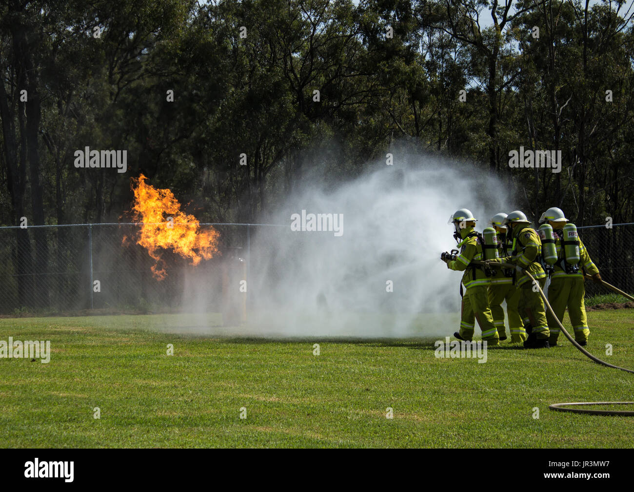 Team of firefighters spraying water on flames in grass field Stock Photo