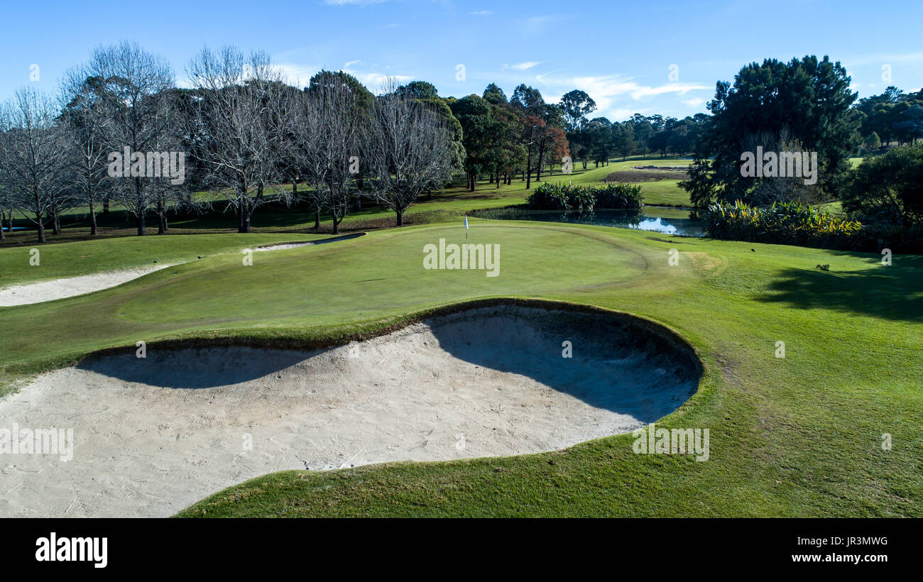 Aerial view of golf course green with flag, bunkers, dam and tree lined fairway in background Stock Photo