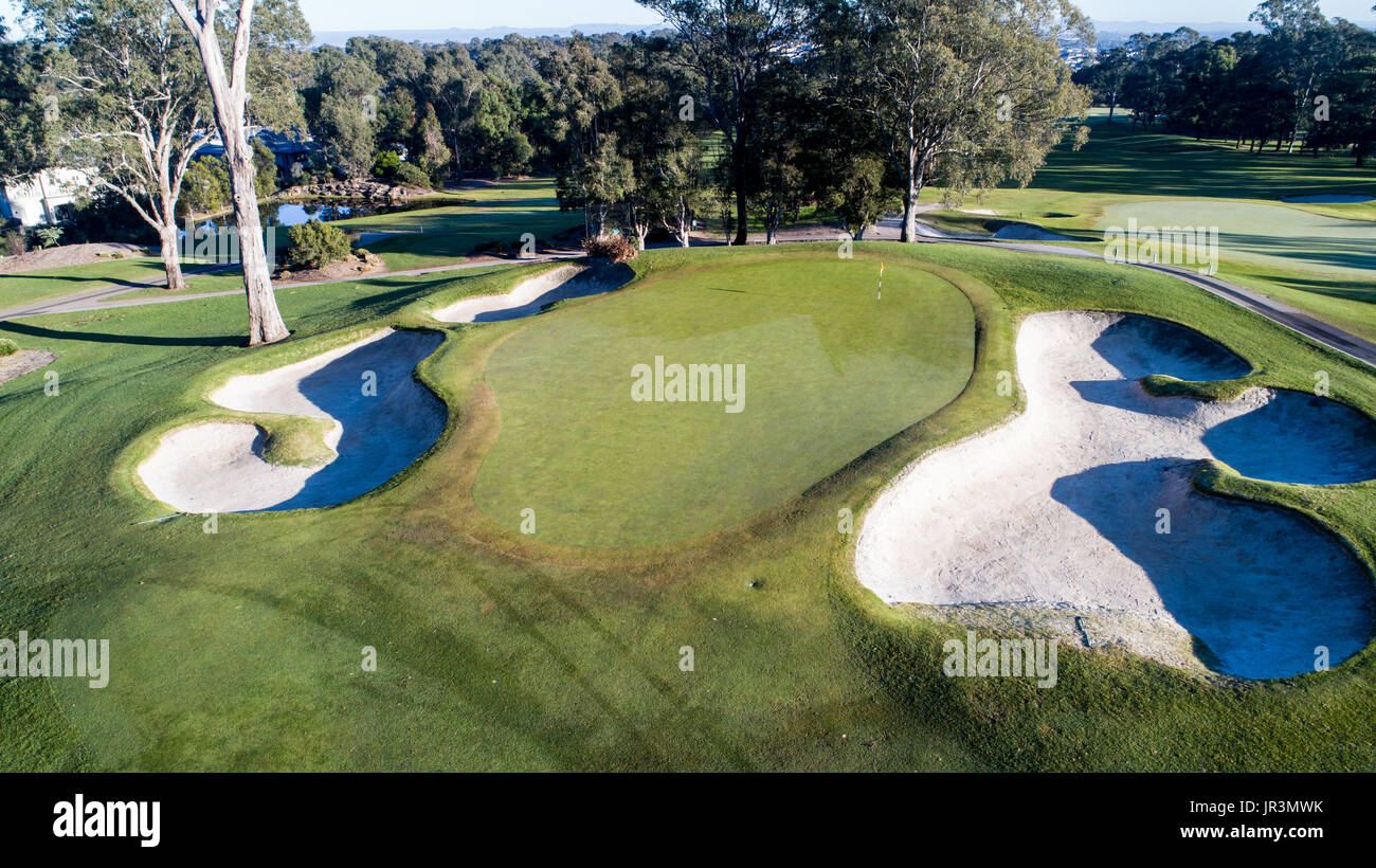 Aerial view of golf course green with flag, bunkers, dam and tree lined fairway in background Stock Photo