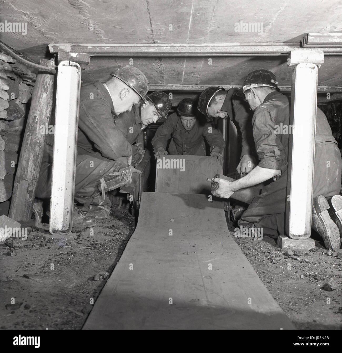1948, historical, male mine workers on their knees laying down flooring in a confined space in an underground coal mine in preparation for the excavation of the minerals. Wooden struts support the low ceiling. Stock Photo