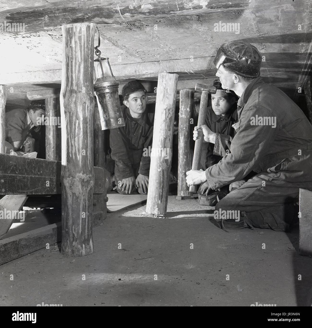 1948, historical, UK, adult coal miner showing young mining trainees or apprentices how timber struts should be used in an underground mine to support the roof structure. Stock Photo