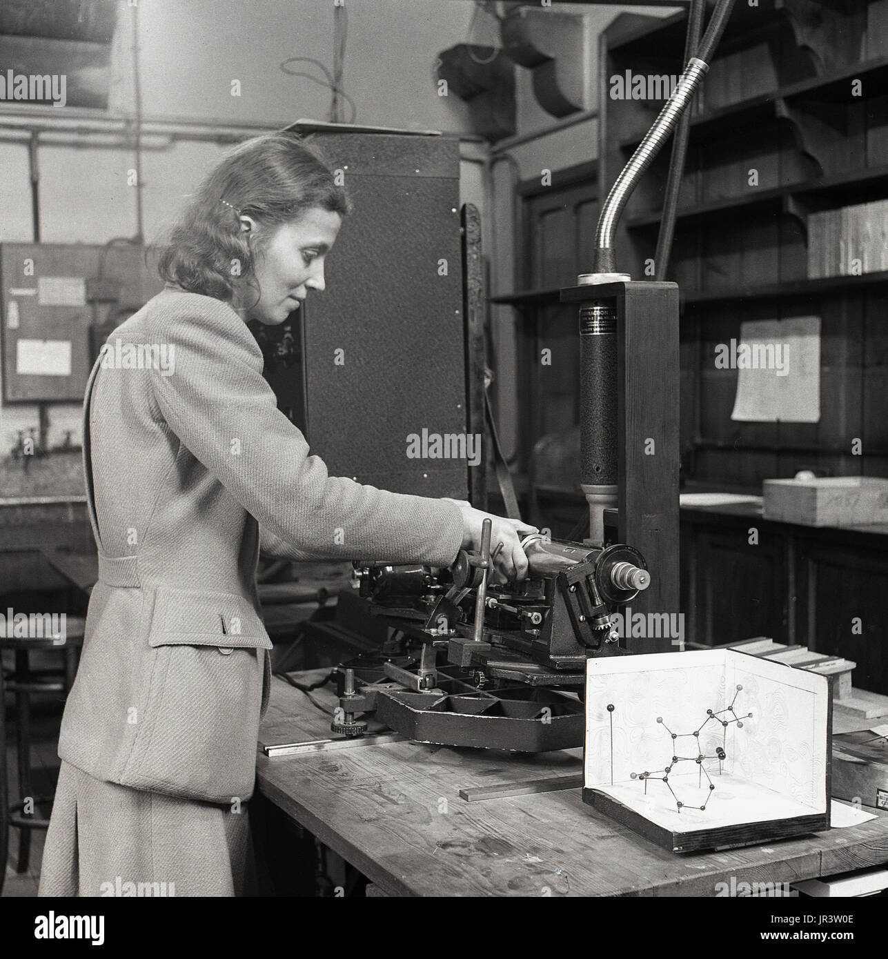 1951, historical, female mathematician in white coat at a workbench doing calculations in a work book using, a ruler, a slide-rule and a ball and stick model, England, UK. Stock Photo