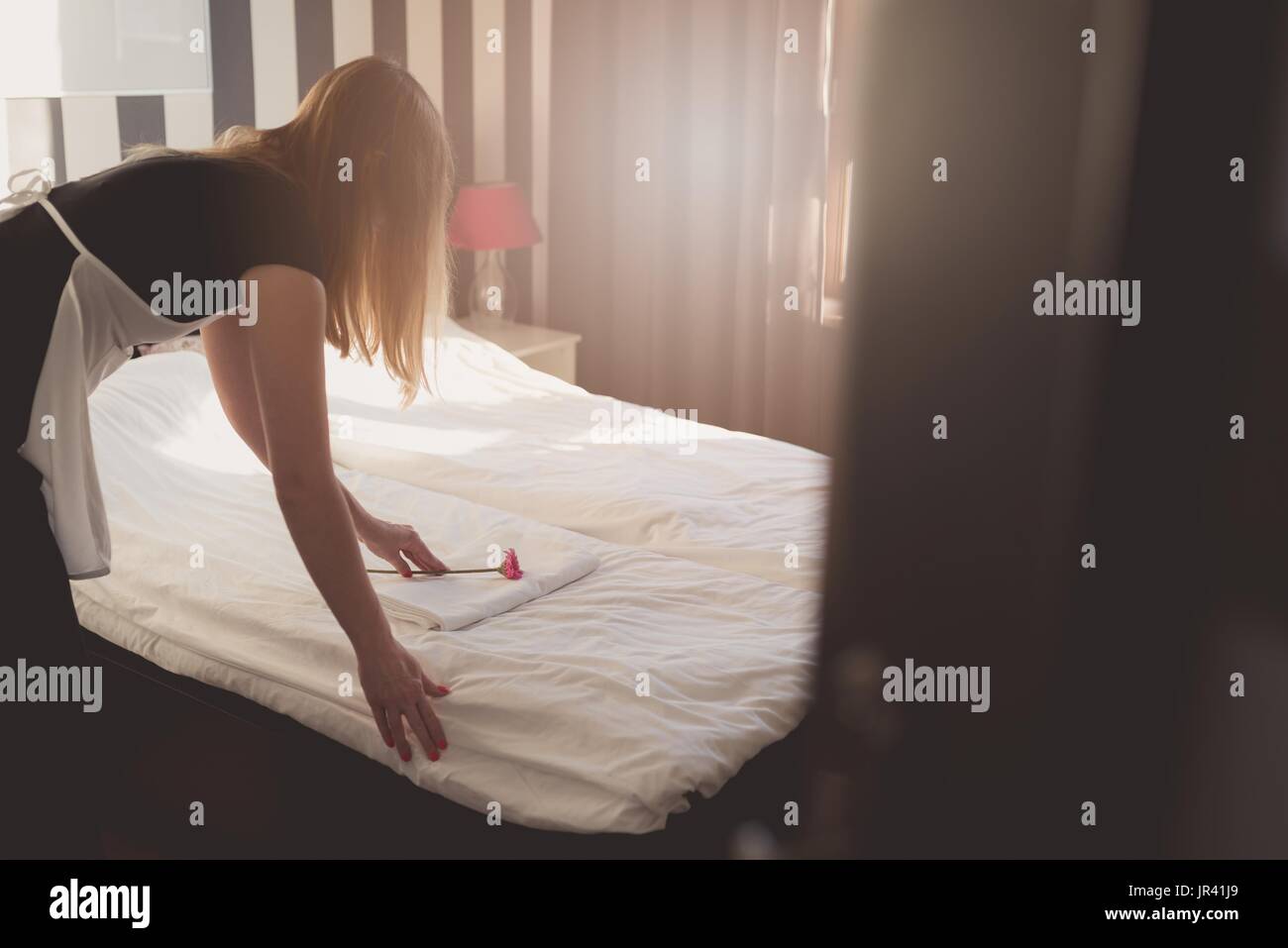 Hotel maid doing room service. She is making up the beds. Stock Photo