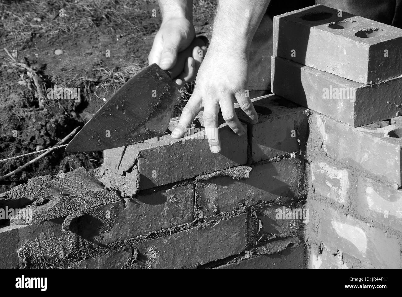 Closeup of bricklayer building a house extension. Photo shows man holding trowel while laying bricks. Stock Photo
