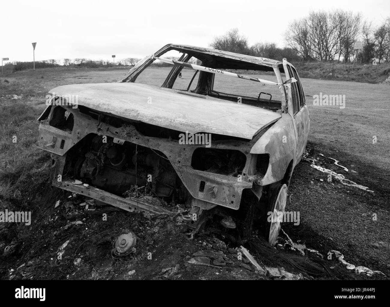 Burnt out abandoned motor car on the side of an isolated road. Stock Photo