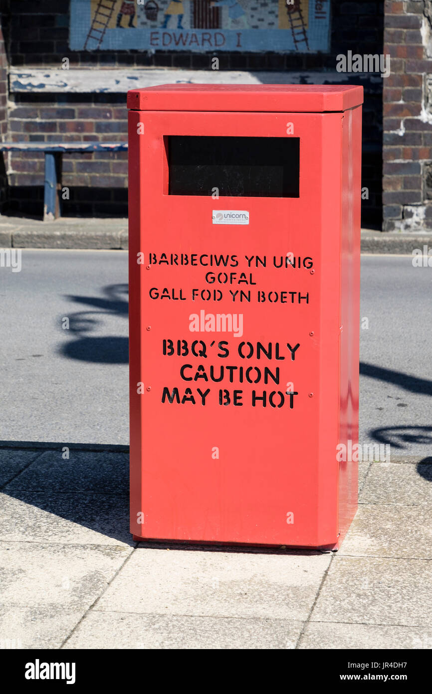 Red rubbish bin on seafront for BBO's only with bilingual wording warning 'caution may be hot'. Aberystwyth, Ceredigion, Wales, UK, Britain Stock Photo