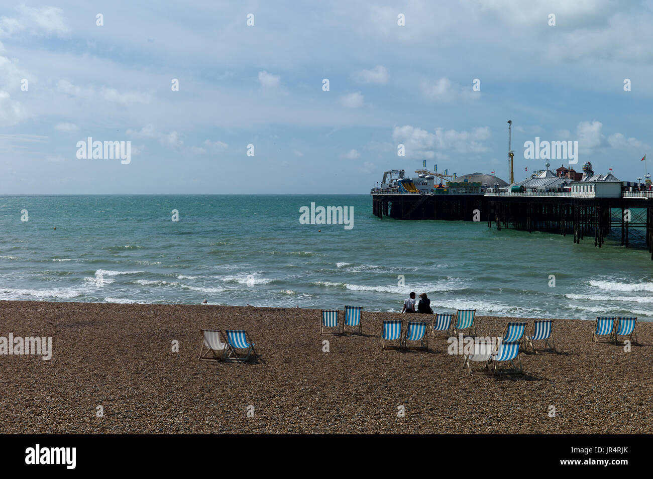 couple sitting on Brighton beach amid empty deckchairs Stock Photo