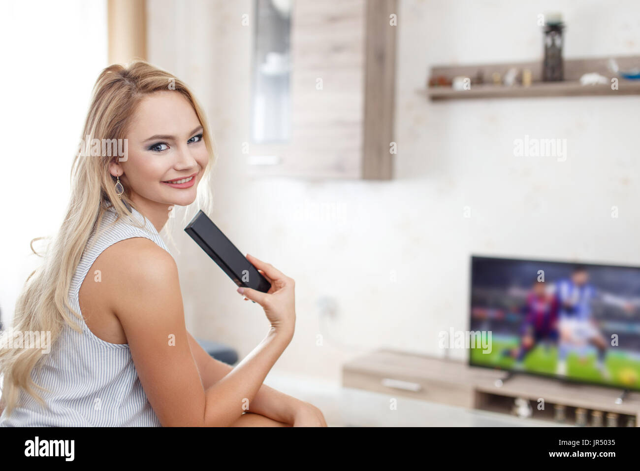 Happy young blonde woman watching soccer in TV Stock Photo