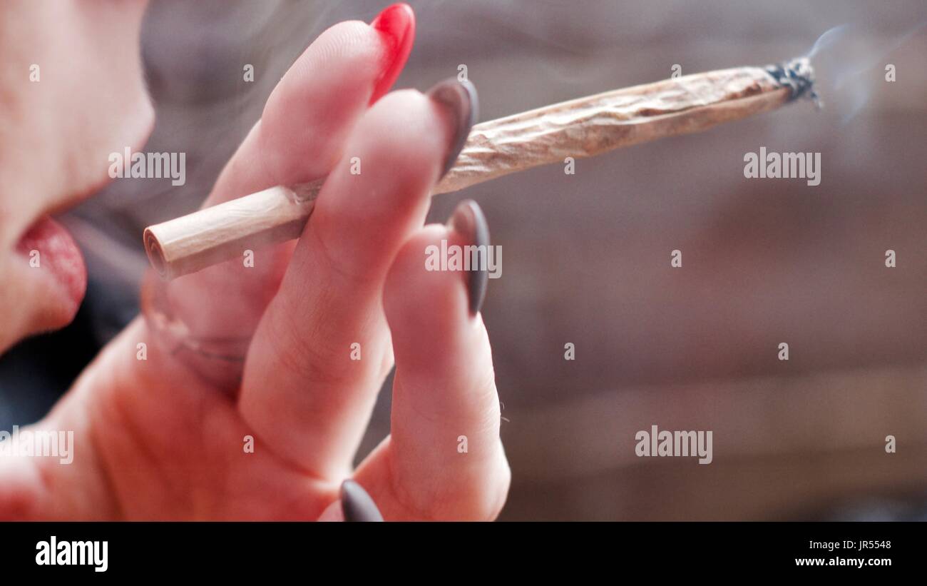 Young woman smoking marijuana spliff and holding in hand with pink and grey nails. Stock Photo