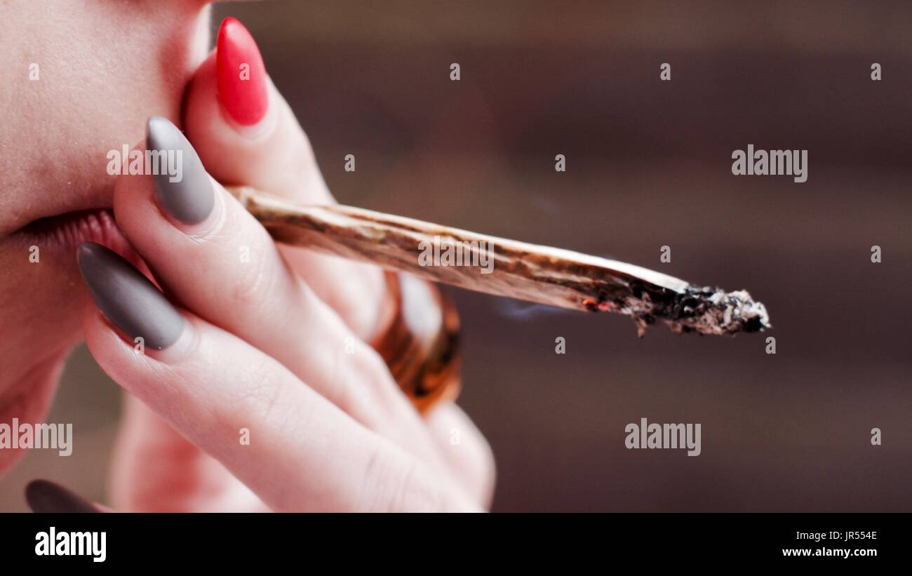 Young white girl smoking marijuana spliff. White hands with pink and grey nails. Stock Photo