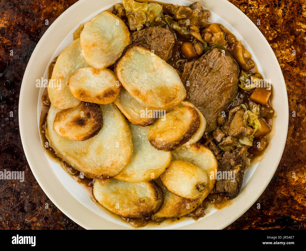 Lamb Hotpot With Sliced Potatoes and Onion Gravy Against a Distressed Burnt Oven or Baking Tray Stock Photo