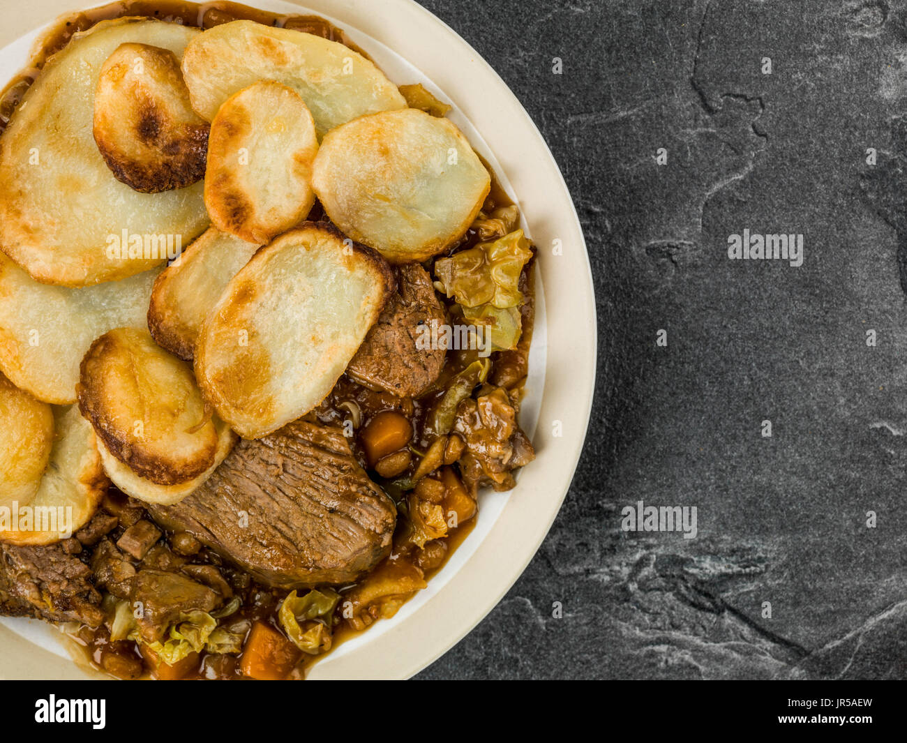 Lamb Hotpot With Sliced Potatoes and Onion Gravy Against a B;ack Slate Tile Background Stock Photo