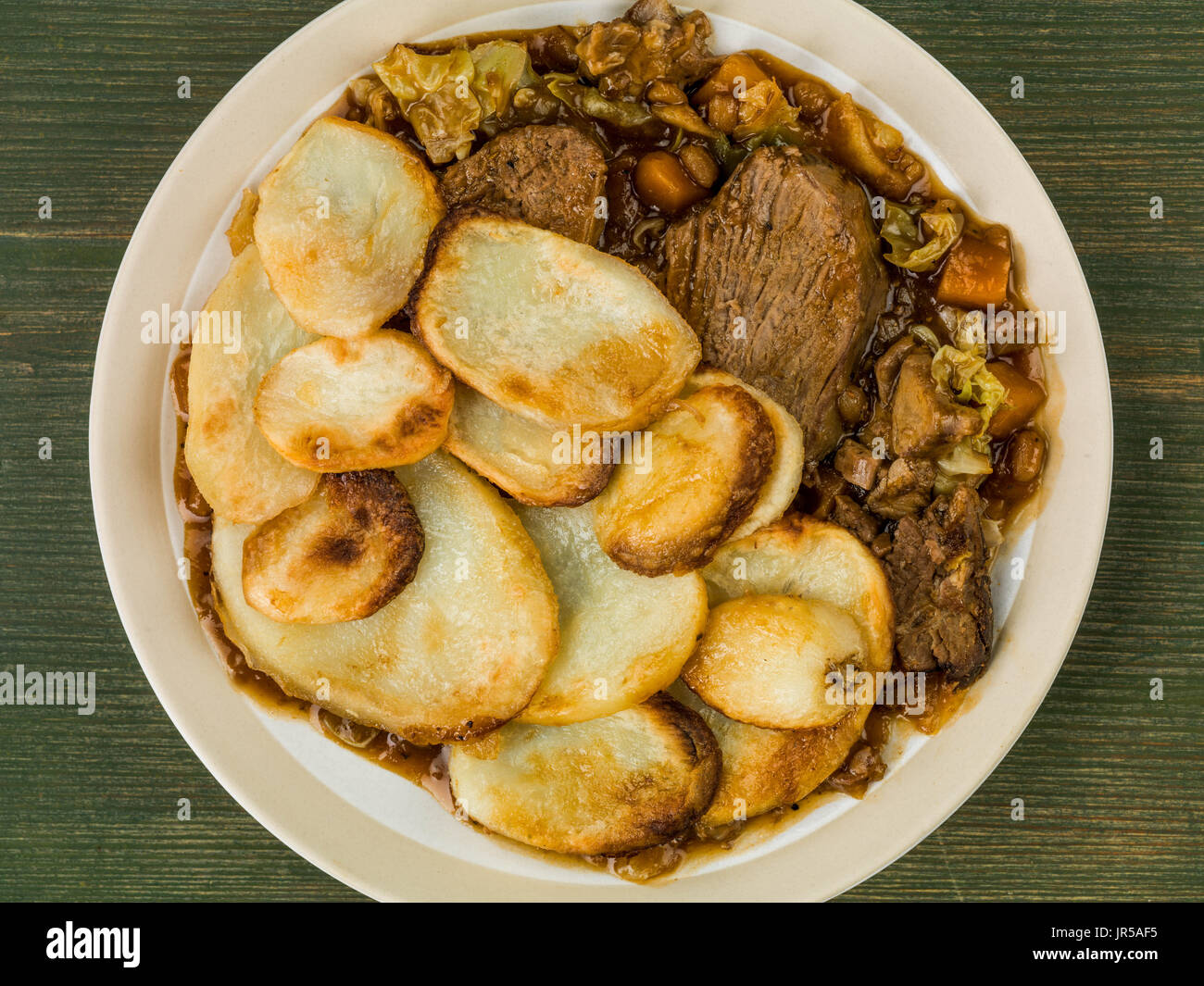 Lamb Hotpot With Sliced Potatoes and Onion Gravy Against a Green Wooden Background Stock Photo