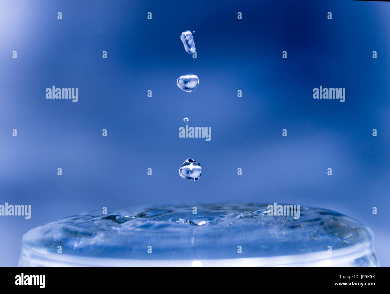 Gotas de agua congeladas con fondo azul y efecto de hielo, bebida refrescante y cristalina, choque y ondas de impacto en el vaso con agua transparente Stock Photo