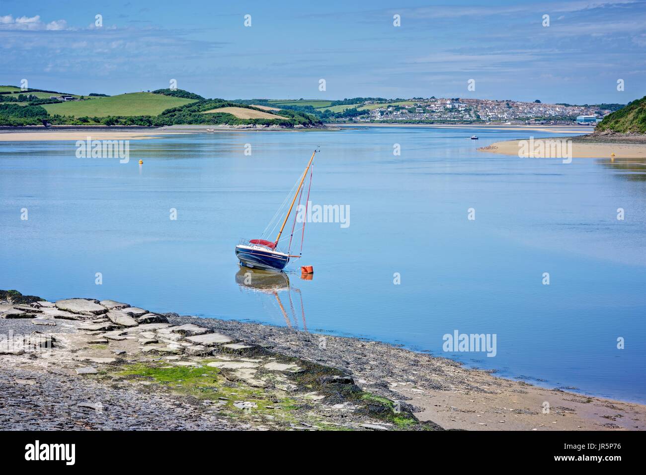 Horizontal landscape of a single boat moored at the shoreline of Cornwall's Camel Estuary with azure blue sea meandering by the Camel Trail to Padstow Stock Photo