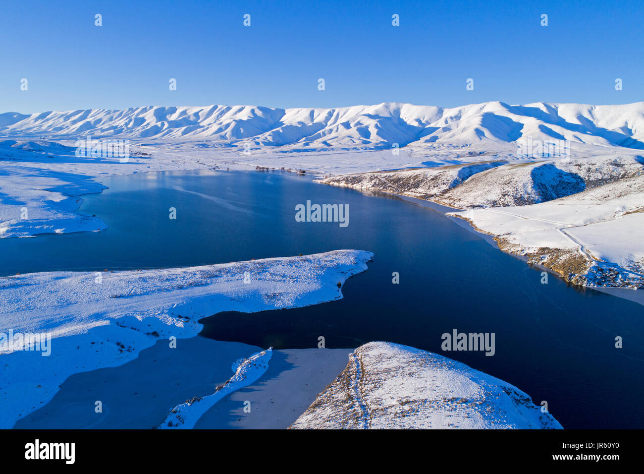 Ice at the edge of Falls Dam, and Hawkdun Range in winter, Maniototo, Central Otago, South Island, New Zealand - drone aerial Stock Photo
