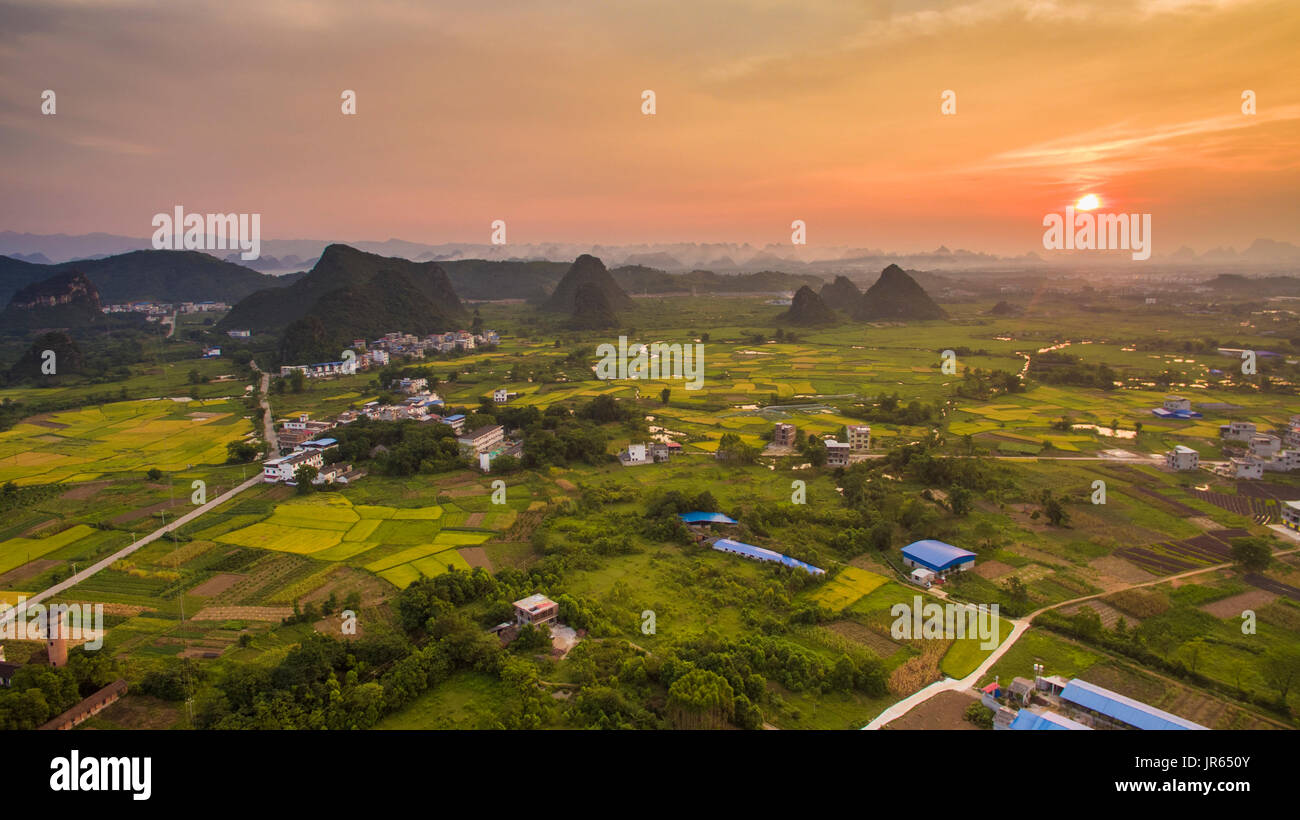 Aerial view of a village surrounded by Padi fields and hills against setting sun in Guanxi, China Stock Photo