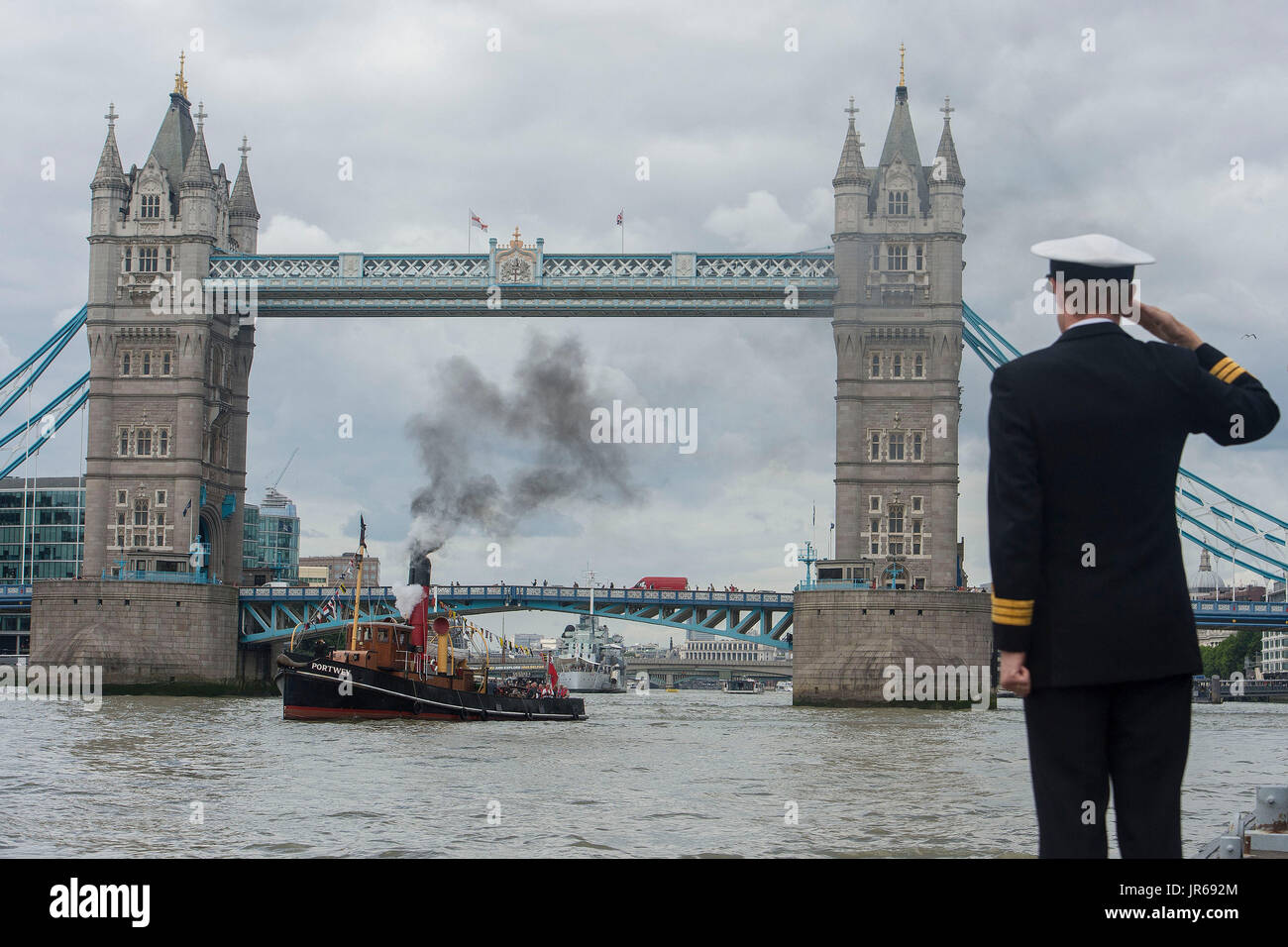 The ST Portwey, a 90-year-old steam tug, which was built on the Clyde in 1927, and which came under command of the Royal Navy during the Second World War, is saluted by Commander Richard Pethybridge as she steams past HMS President, the Royal Navy's permanent shore establishment on the River Thames in London, as they mark the tugs 90th birthday. Stock Photo