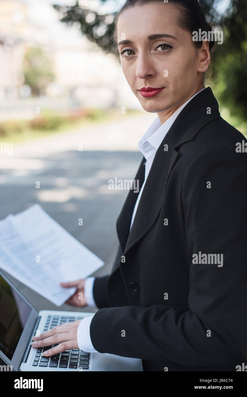 Businesswoman sitting on bench working on her laptop computer Stock Photo