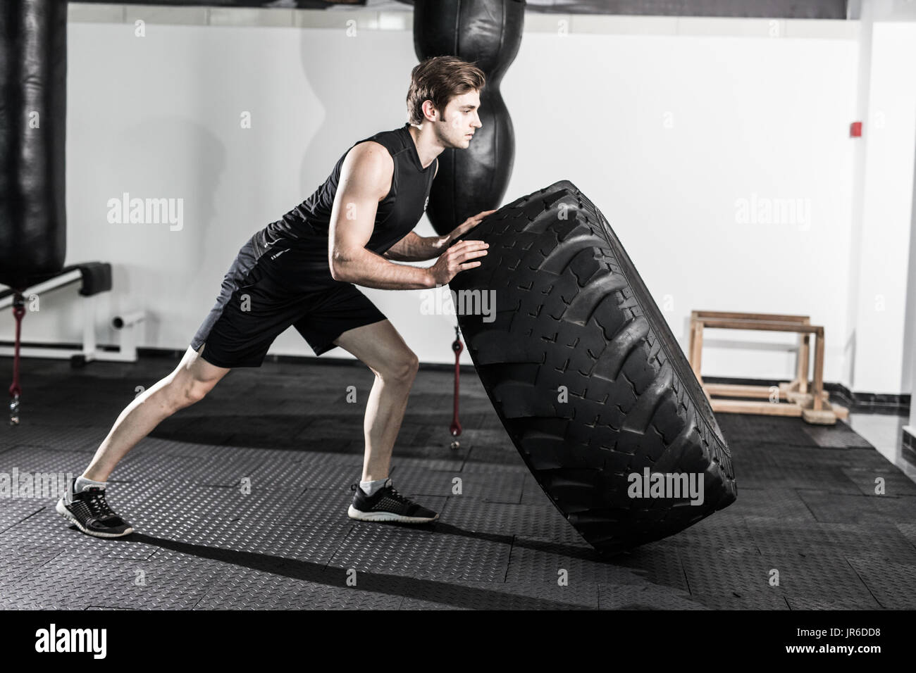 Personal trainer flipping a tyre in a dark gym while instructing a female fitness model how to do the exercise Stock Photo Alamy