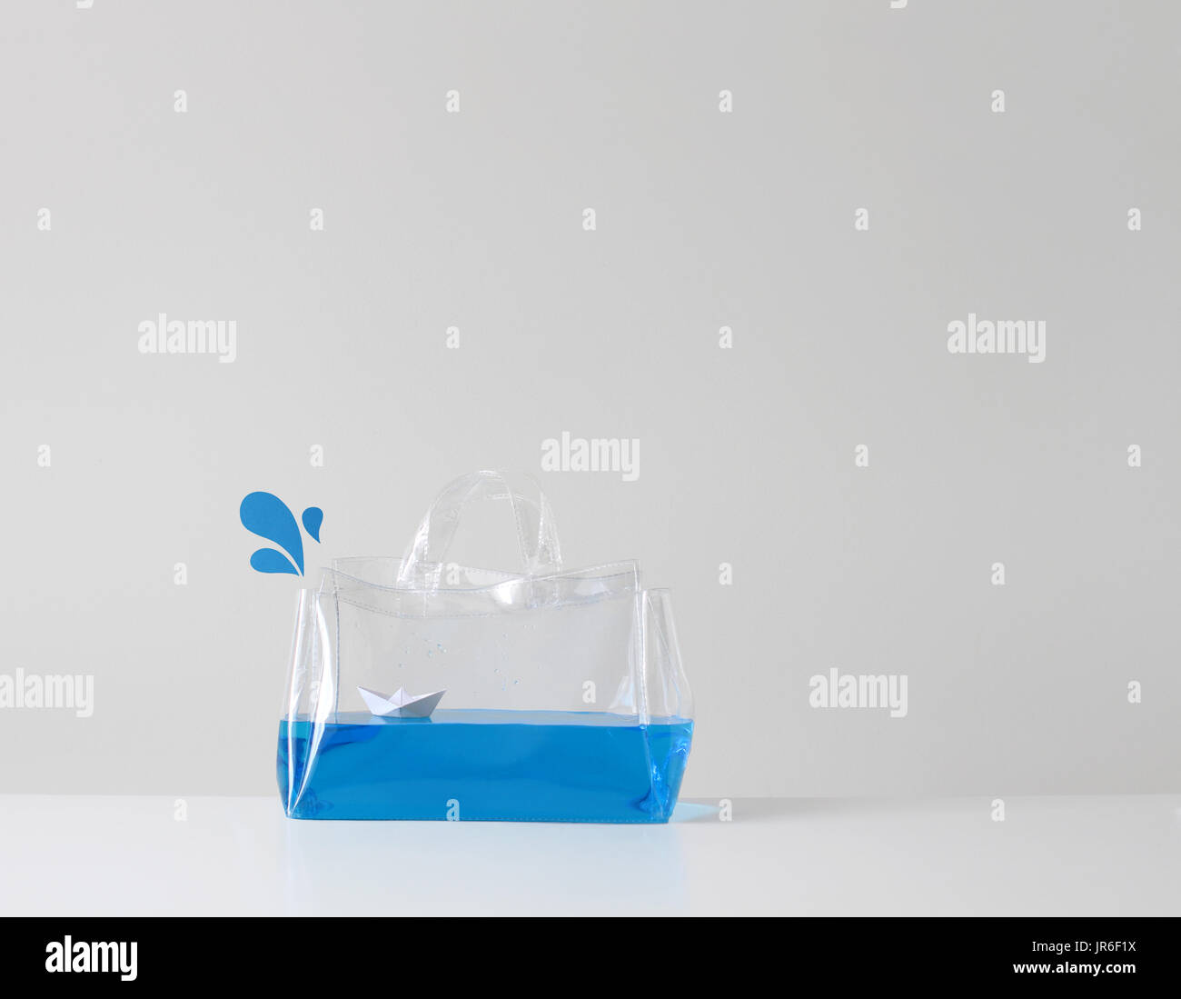 Paper boat floating on blue water in a transparent plastic bag Stock Photo