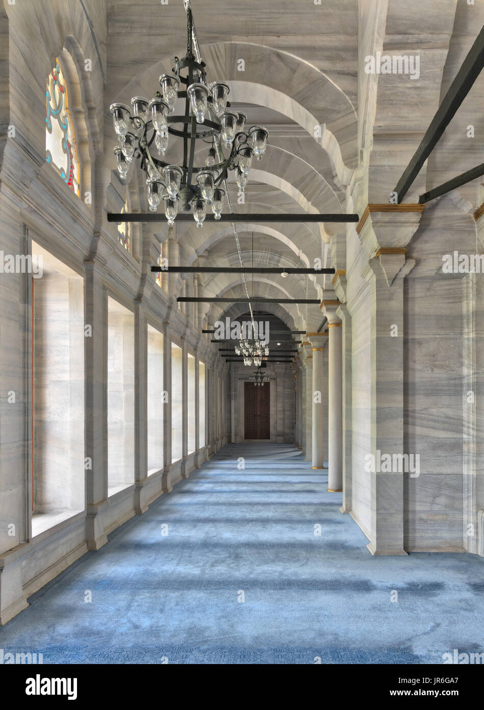 Passage in Nuruosmaniye Mosque, a public Ottoman Baroque style mosque, with columns, arches and floor covered with blue carpet lighted by side windows Stock Photo