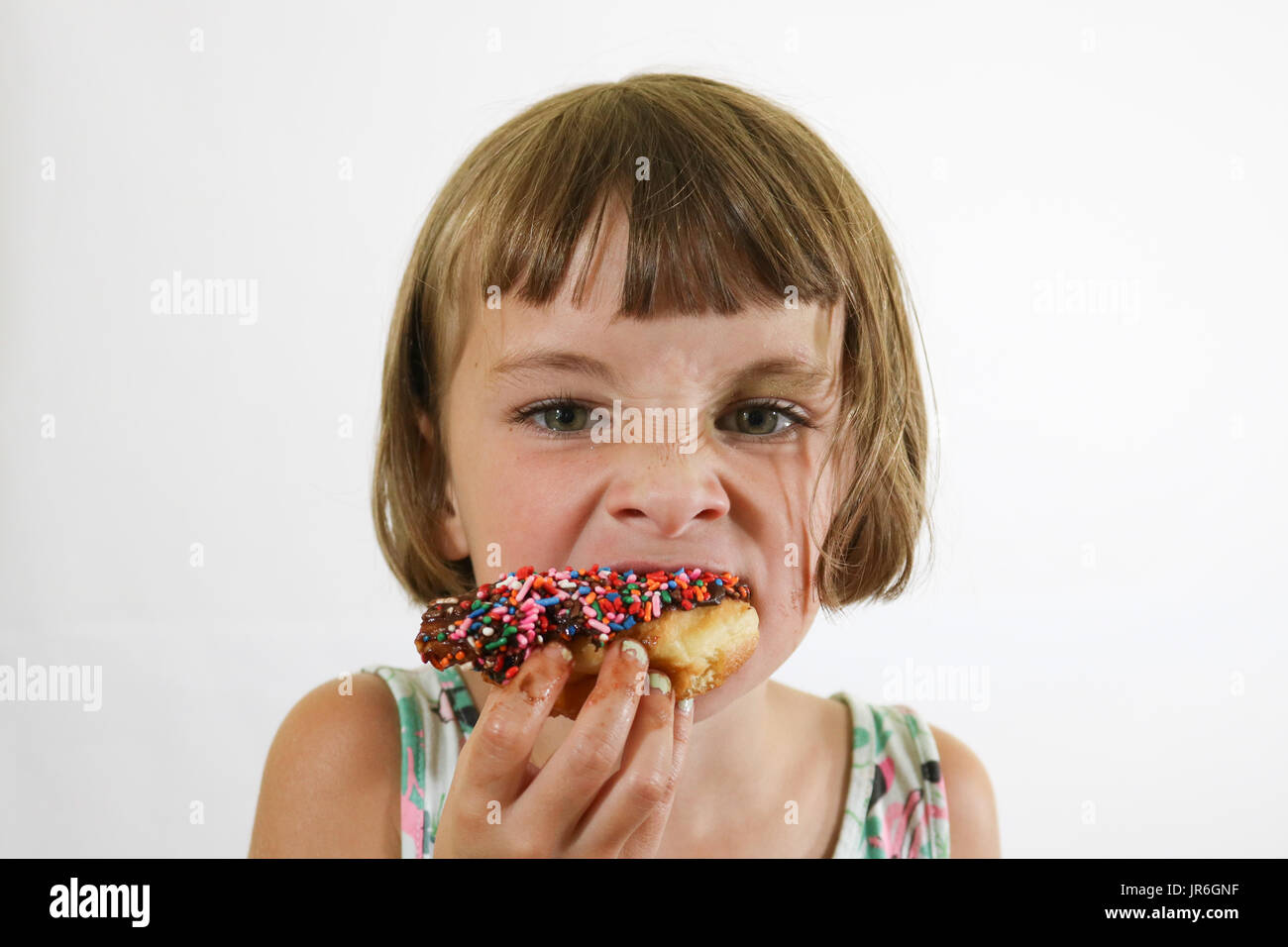 Portrait of a little brown haired girl eating a donut with colorful sprinkles Stock Photo