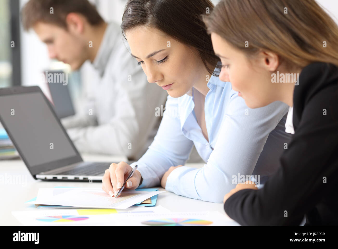 Close up of two concentrated employees coworking analyzing data in paper documents at office Stock Photo
