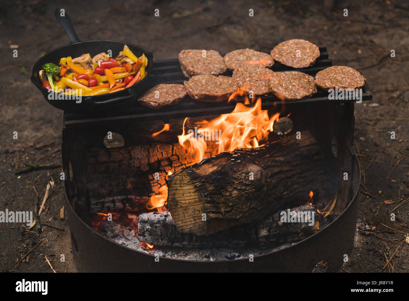 Hamburgers and vegetables cooking on a barbecue on camp fire Stock Photo