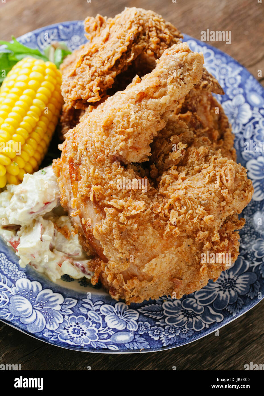 Buttermilk fried chicken with corn and potato salad on a blue plate