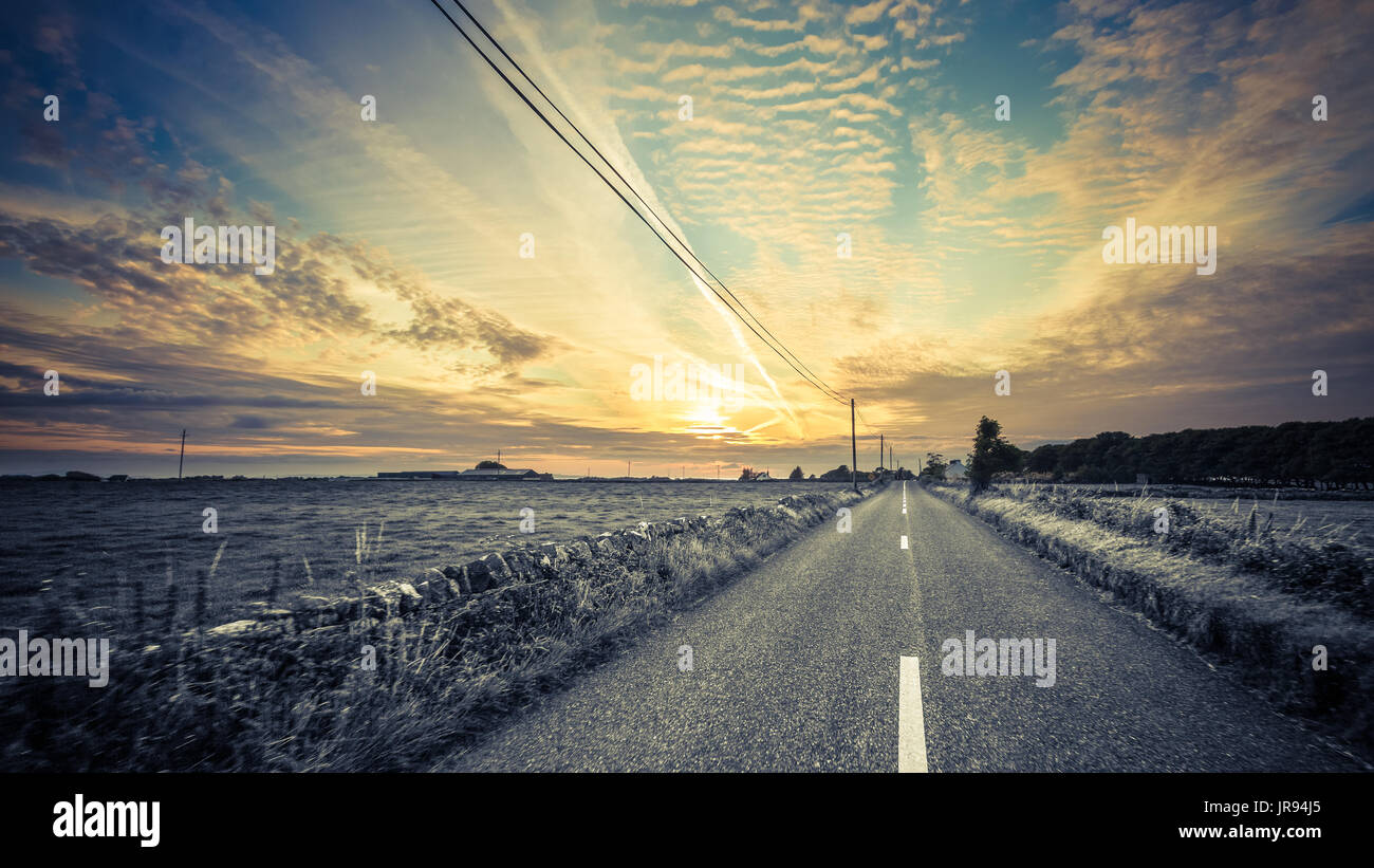 Drivers view of a long straight road with a nice sunset to look at. Stock Photo