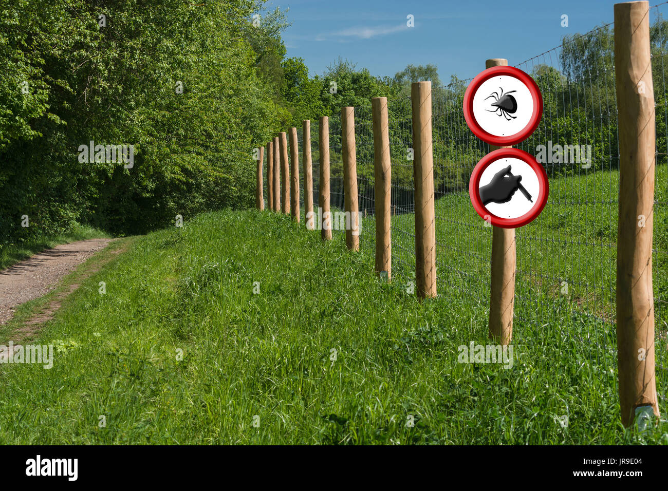 Borreliosis and tick warning. Two round red warning signs on a fence post in front of a green meadow. A sign with ticks symbol the other shows a hand  Stock Photo