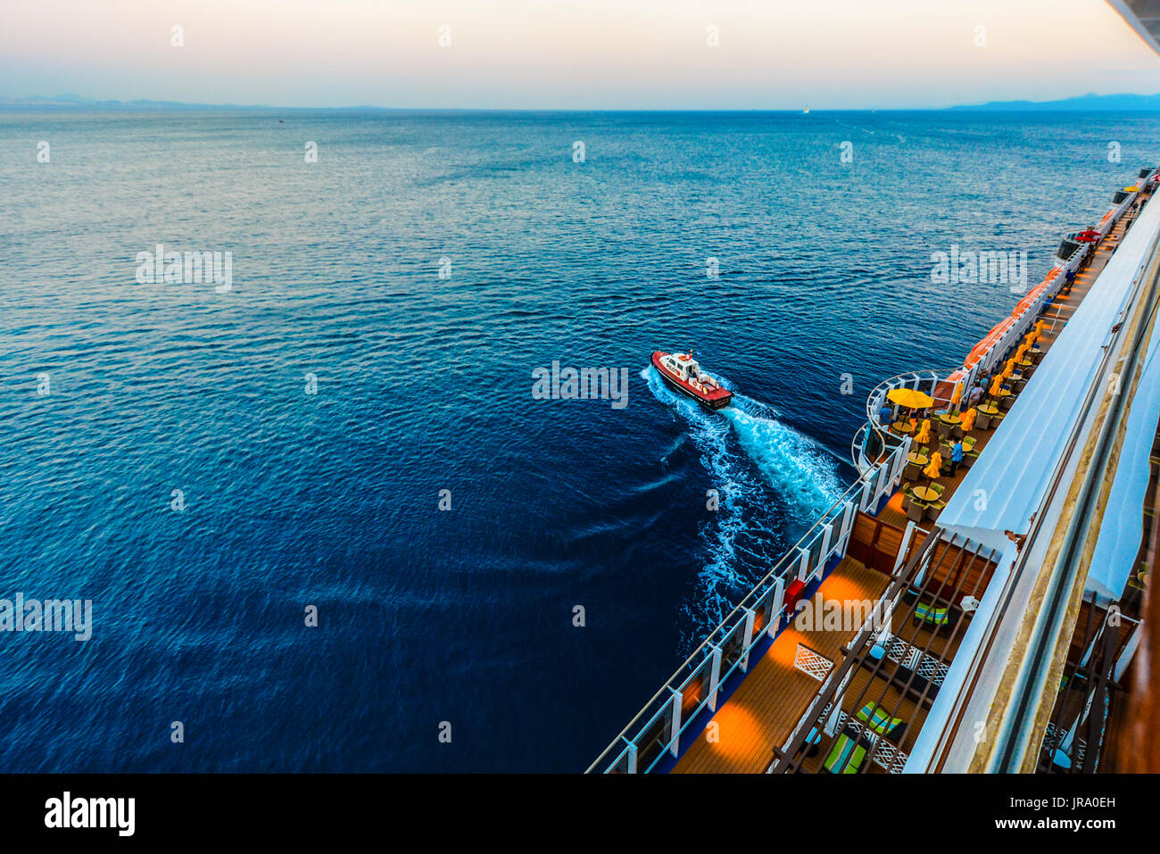 Small pilot boat pulling away from a large cruise ship at departure in the Mediterranean sea Stock Photo