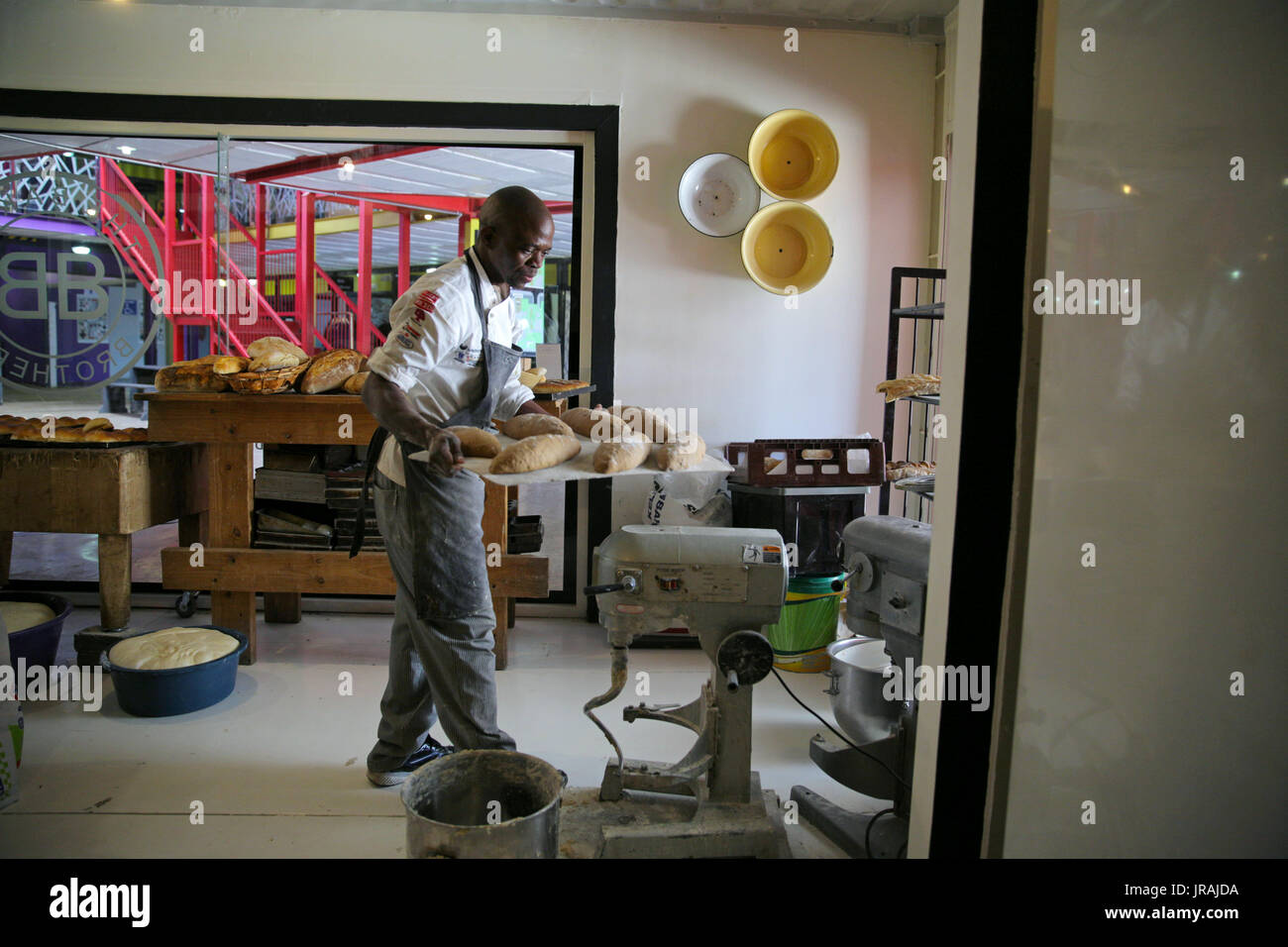 African baker carrying tray of loaves of bread in bakery Stock Photo