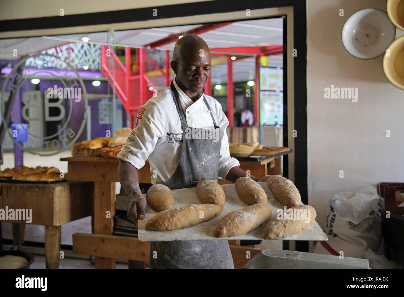 African baker carrying tray of loaves of bread in bakery Stock Photo