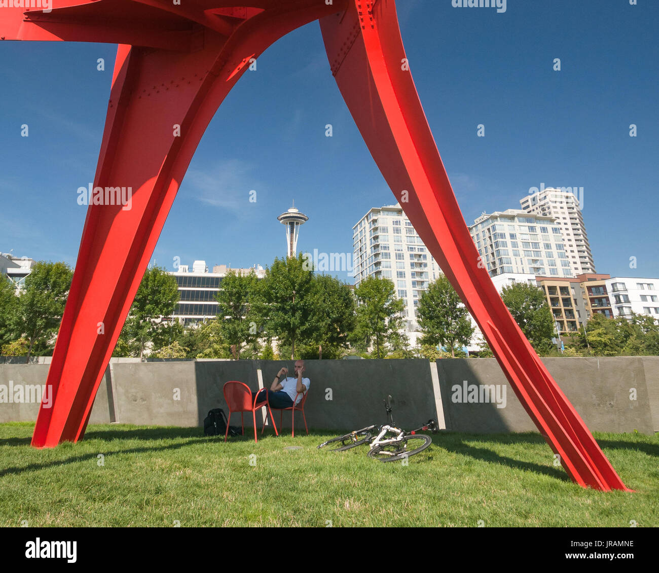 Seattle Space Needle seen from the Olympic Sculpture Park where a cyclist rests in the shade of The Eagle Stock Photo