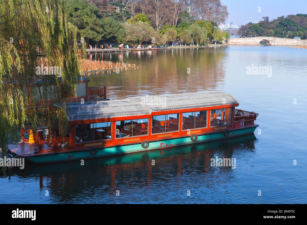 Traditional Chinese red wooden recreational boat stands moored on the West Lake coast. Famous public park in Hangzhou city, China Stock Photo