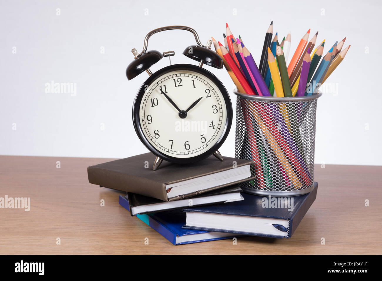 Alarm clock standing on pile of planners with colored pencils in container Stock Photo