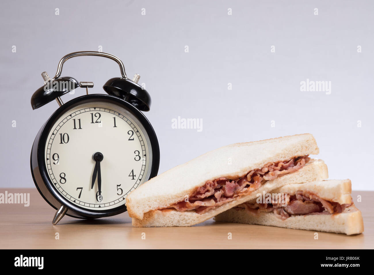 Alarm clock standing by sandwich with meat on table Stock Photo