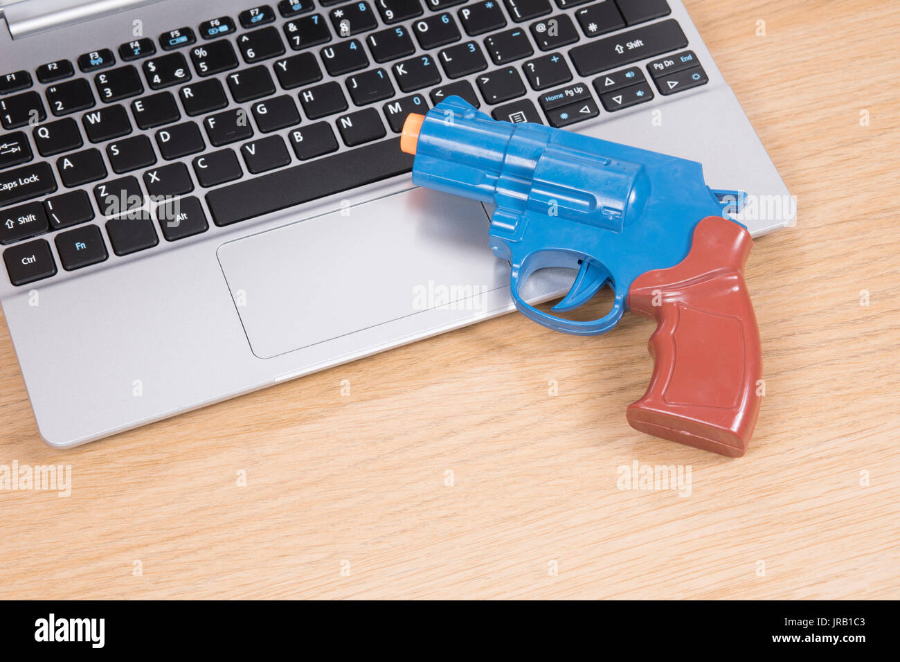 Colorful toy handgun lying on a laptop computer in a concept of online ransomware, fraud, crime, or identity theft and hacking Stock Photo